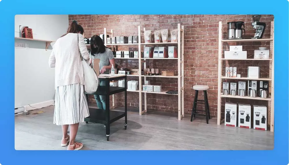 Two people at a counter in a stylish brick-walled coffee shop with products on display.