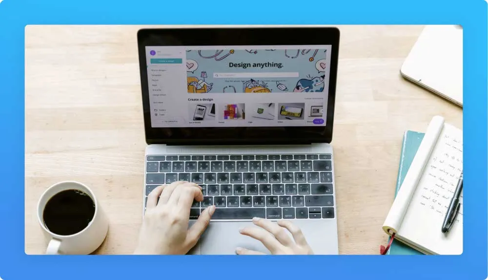Tech worker developing a product at the laptop. Screen shows a banner with "Design anything". Coffee mug and notebooks each side of the laptop.