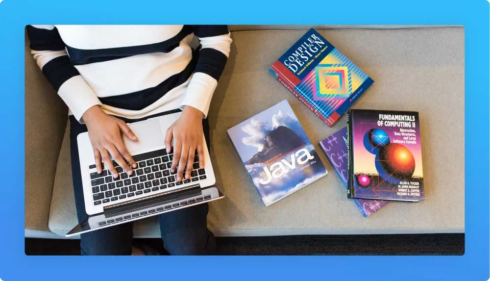 Person on couch using laptop, 4 programming and design related books on the side