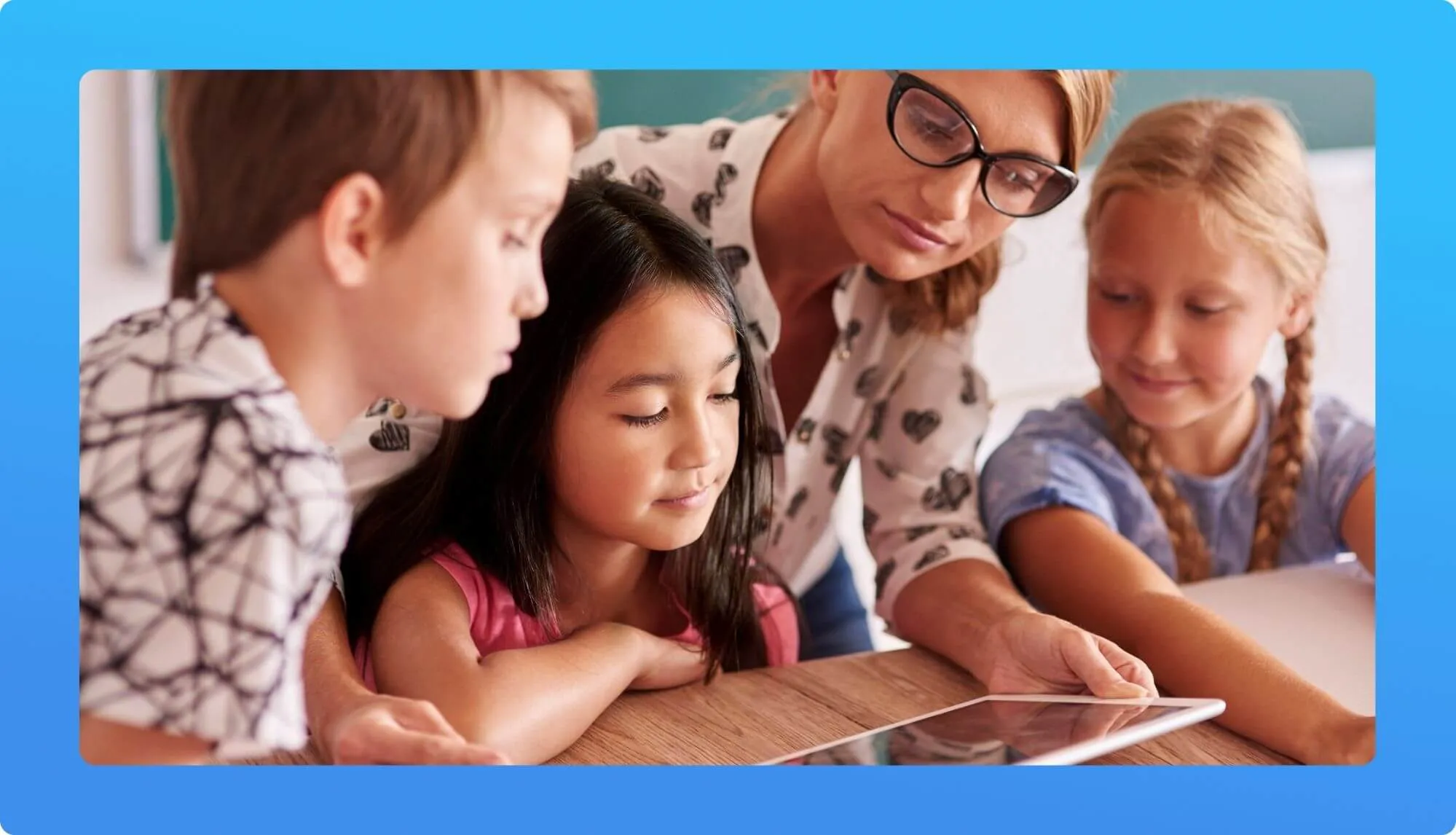 A group of children and an adult gather around a tablet on a wooden table, engaged in a learning activity together.