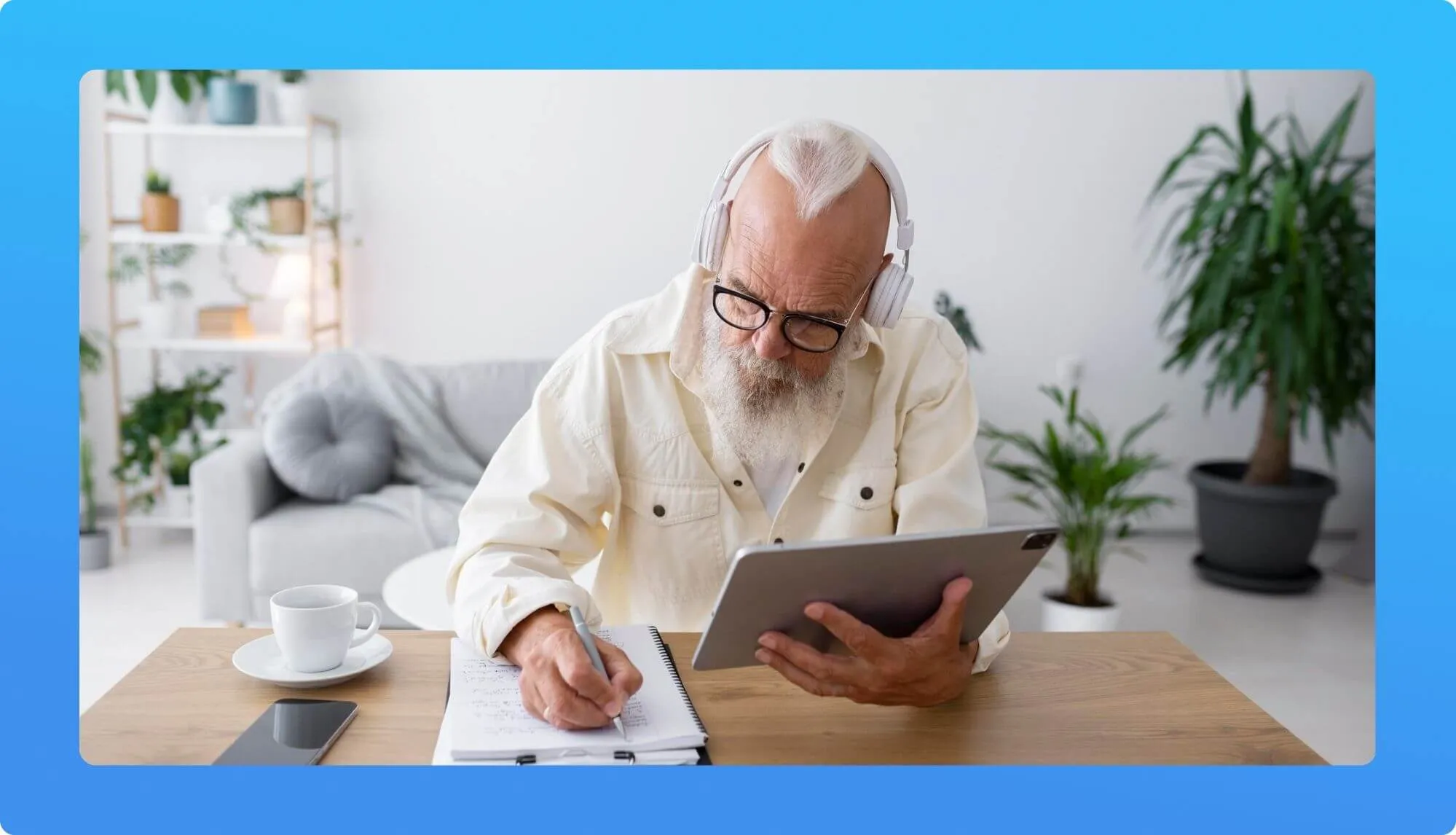 An elderly individual wearing headphones, focusing on a tablet, with a notebook, pen, and a cup of coffee on a wooden table, surrounded by plants.