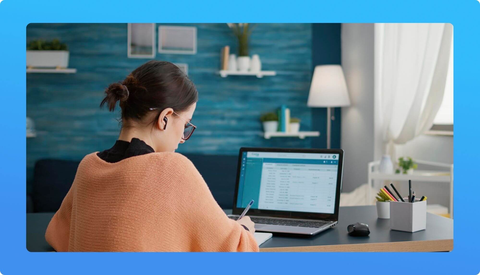 A person seated at a desk, focused on a laptop displaying data, with home office decor including a lamp and potted plants.