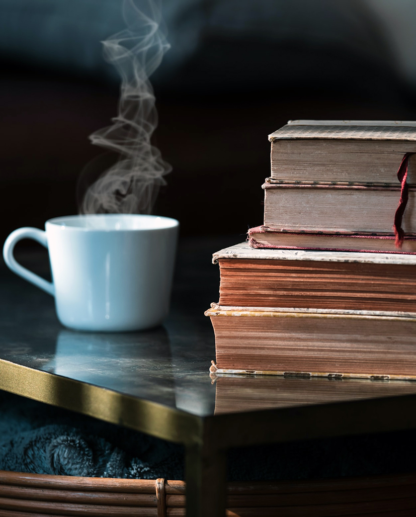Eine dampfende Tasse Kaffee auf einem dunklen Beistelltisch neben einem Stapel alter Bücher.