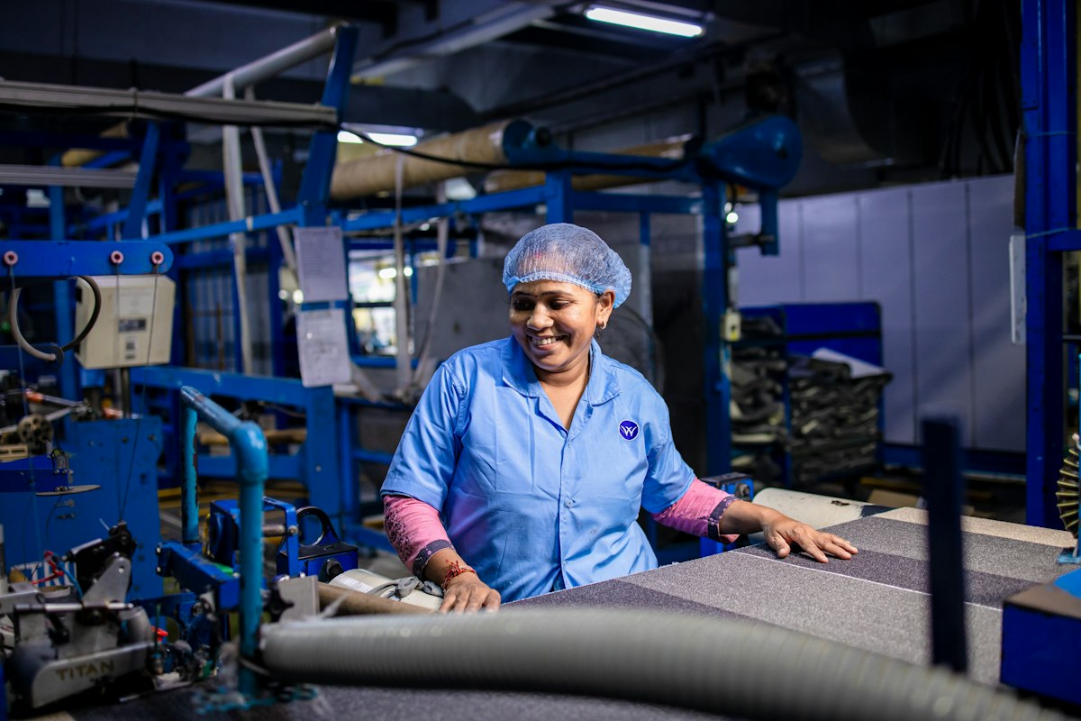 Eine Frau in Arbeitskleidung lacht bei der Arbeit in einer Fabrik.