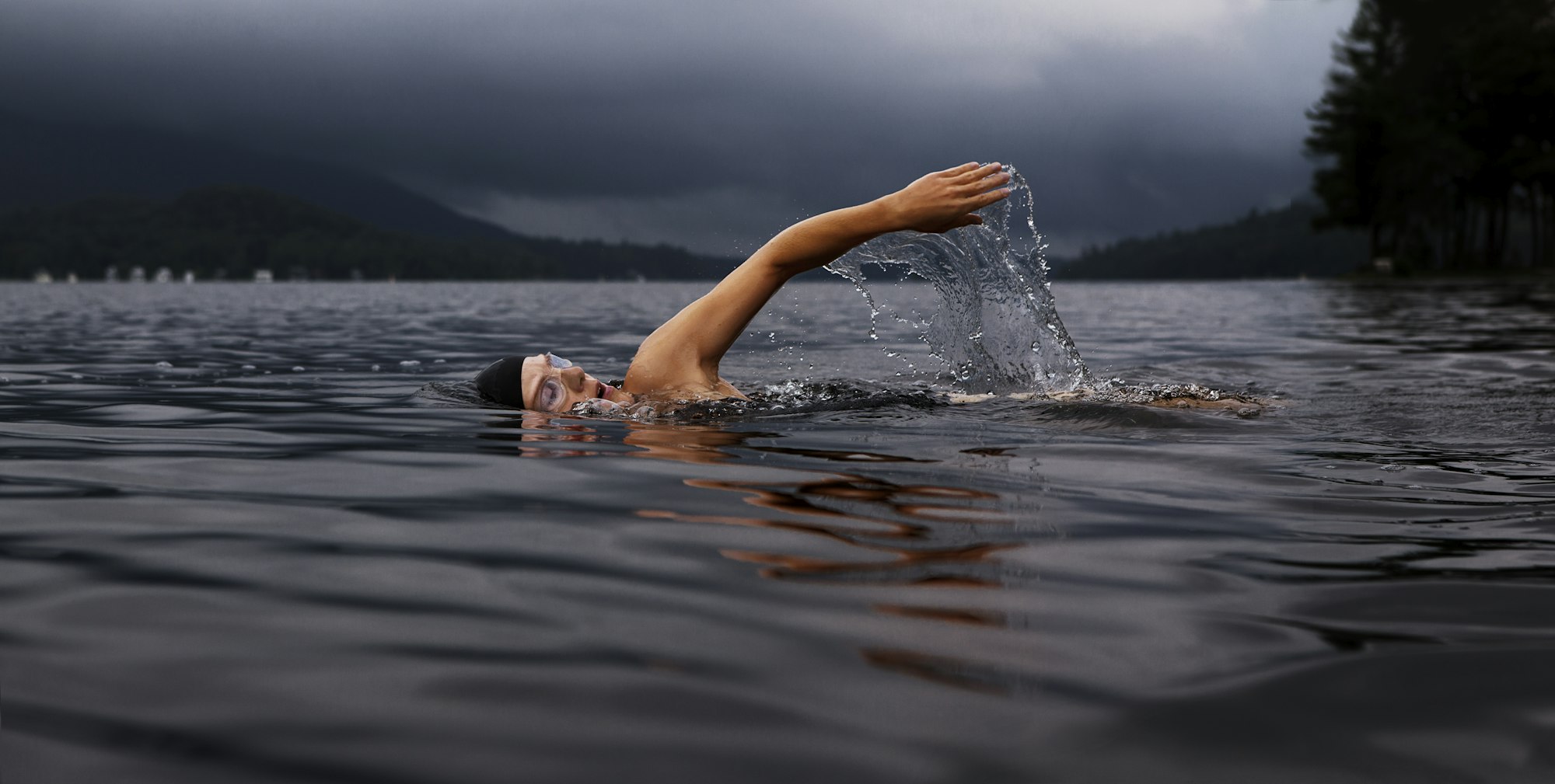 Ein Mensch schwimmt allein durch einen dunklen See, ein Arm hebt sich aus dem Wasser.