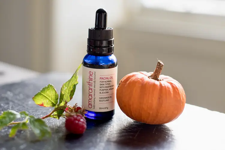 Amaranthine natural face oil bottle with pumpkin seed oil beside a small pumpkin and raspberry, highlighting autumn skincare and nourishing botanicals.