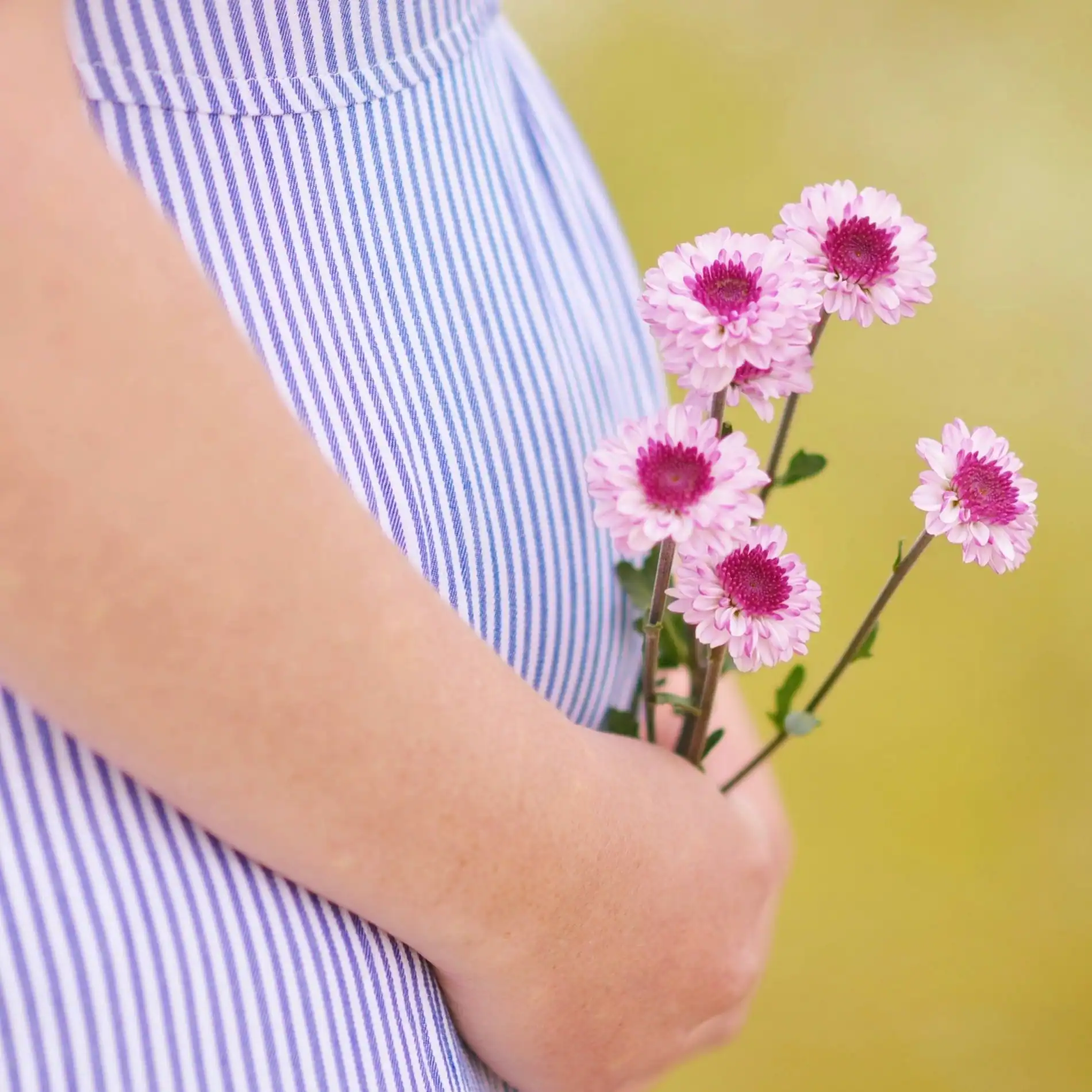 Pregnant woman holding flowers, representing gentle self-care during pregnancy.