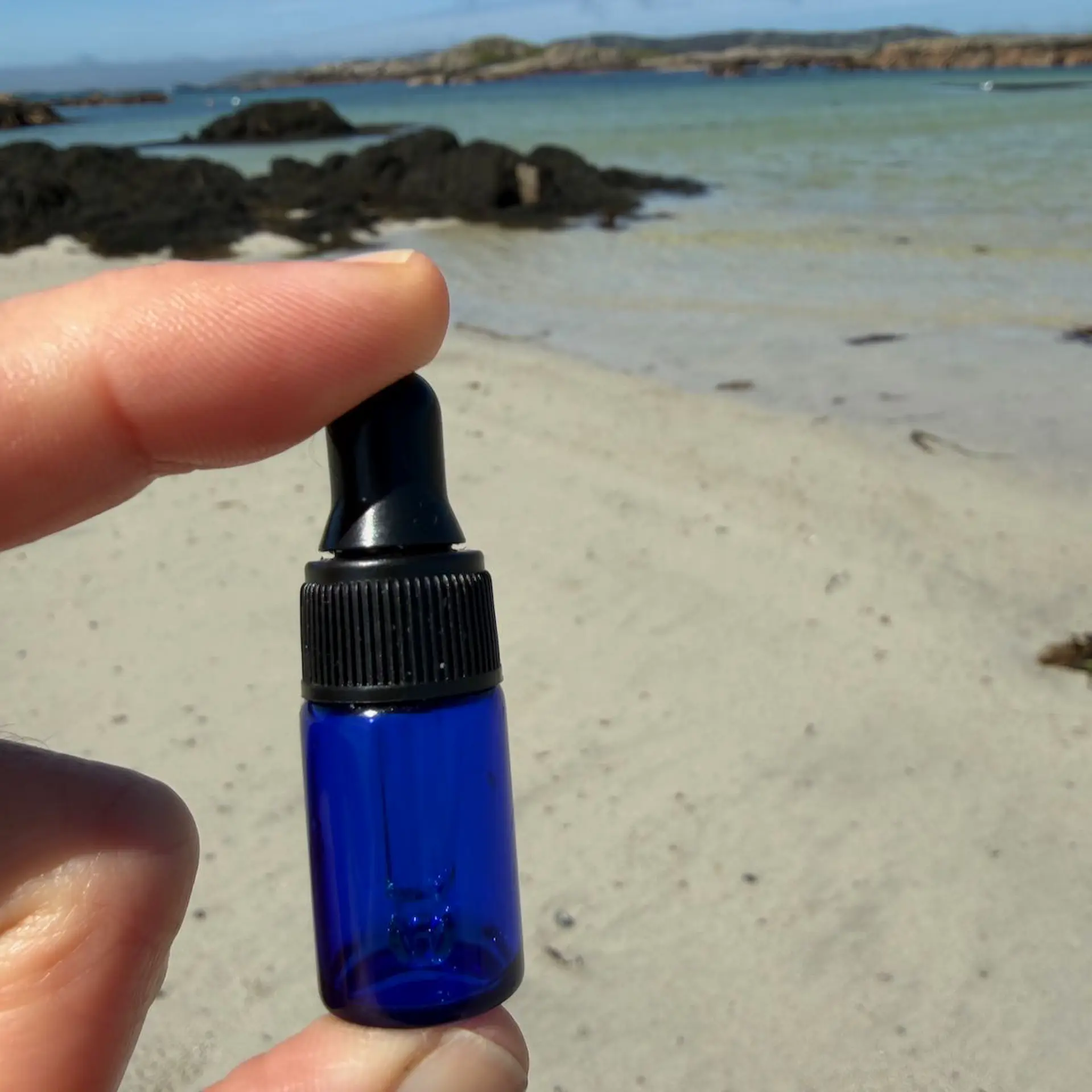 Blue glass mini refillable face oil bottle with beach background.
