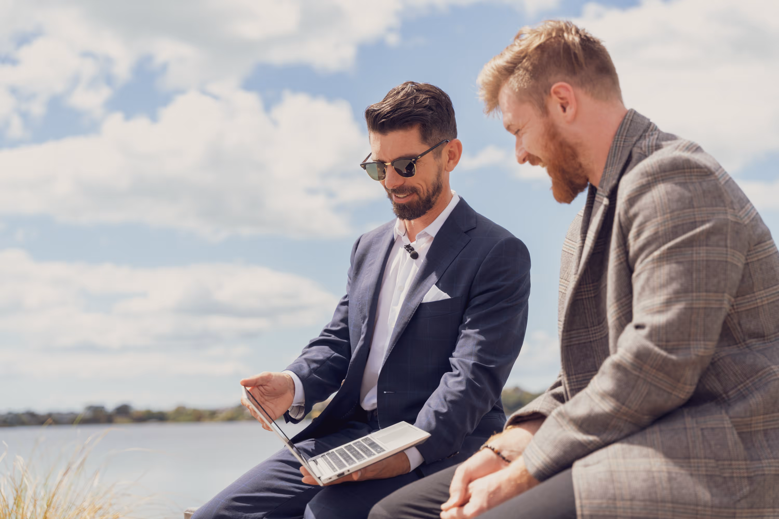 Two men in suits talking outdoors by the water