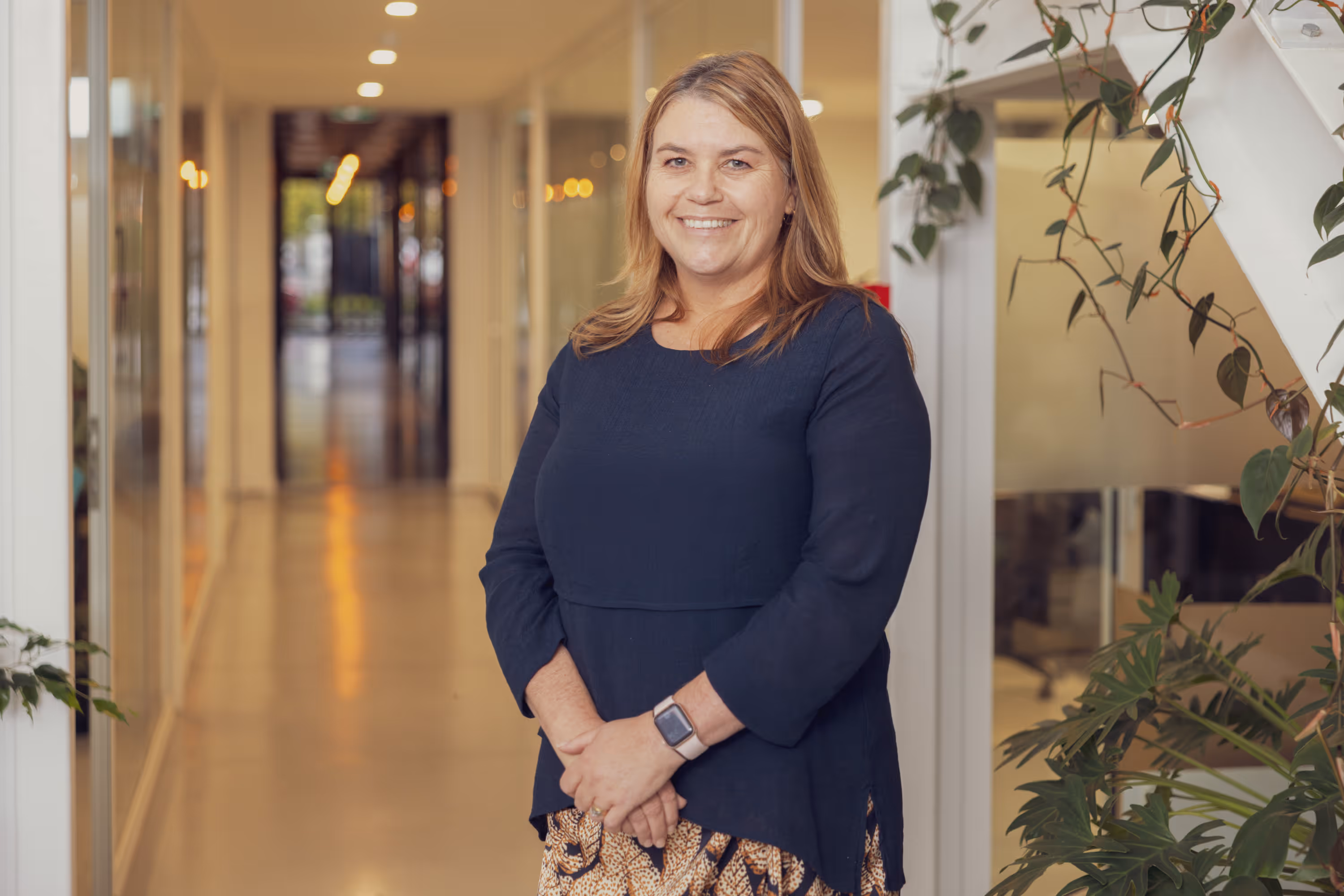 Woman standing in a modern office hallway smiling