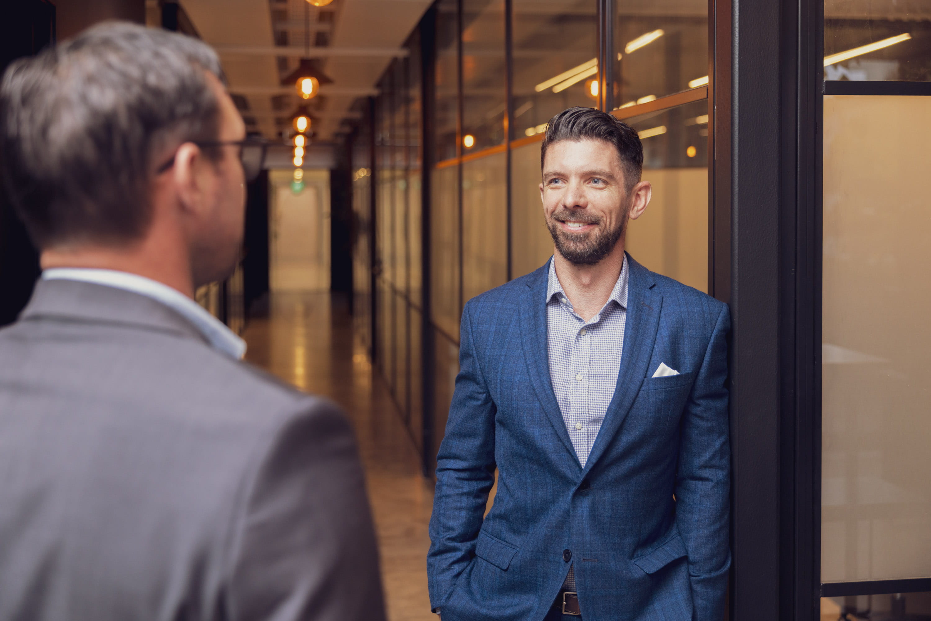 Joseph (CEO) talks to Marcus (financial adviser) in a Become Wealth hallway