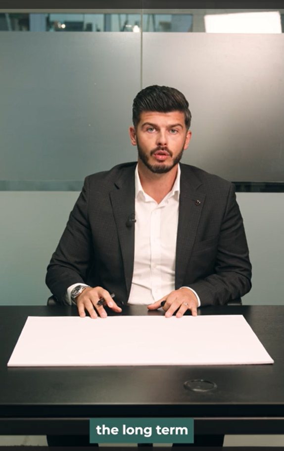 Nik (financial adviser) seated with a whiteboard marker, about to explain an investing concept