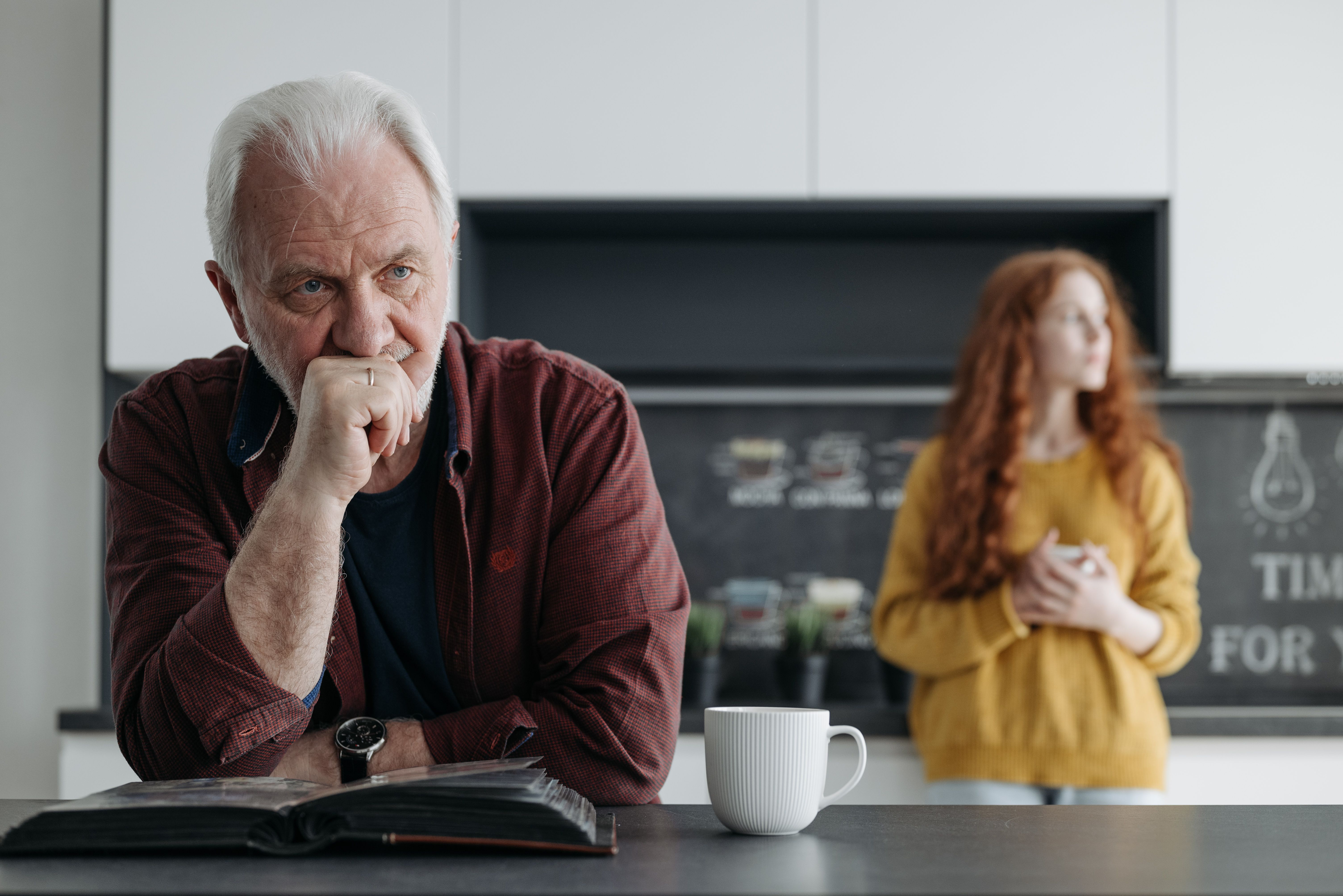 Age gap couple: older man, in focus. Younger woman in the background