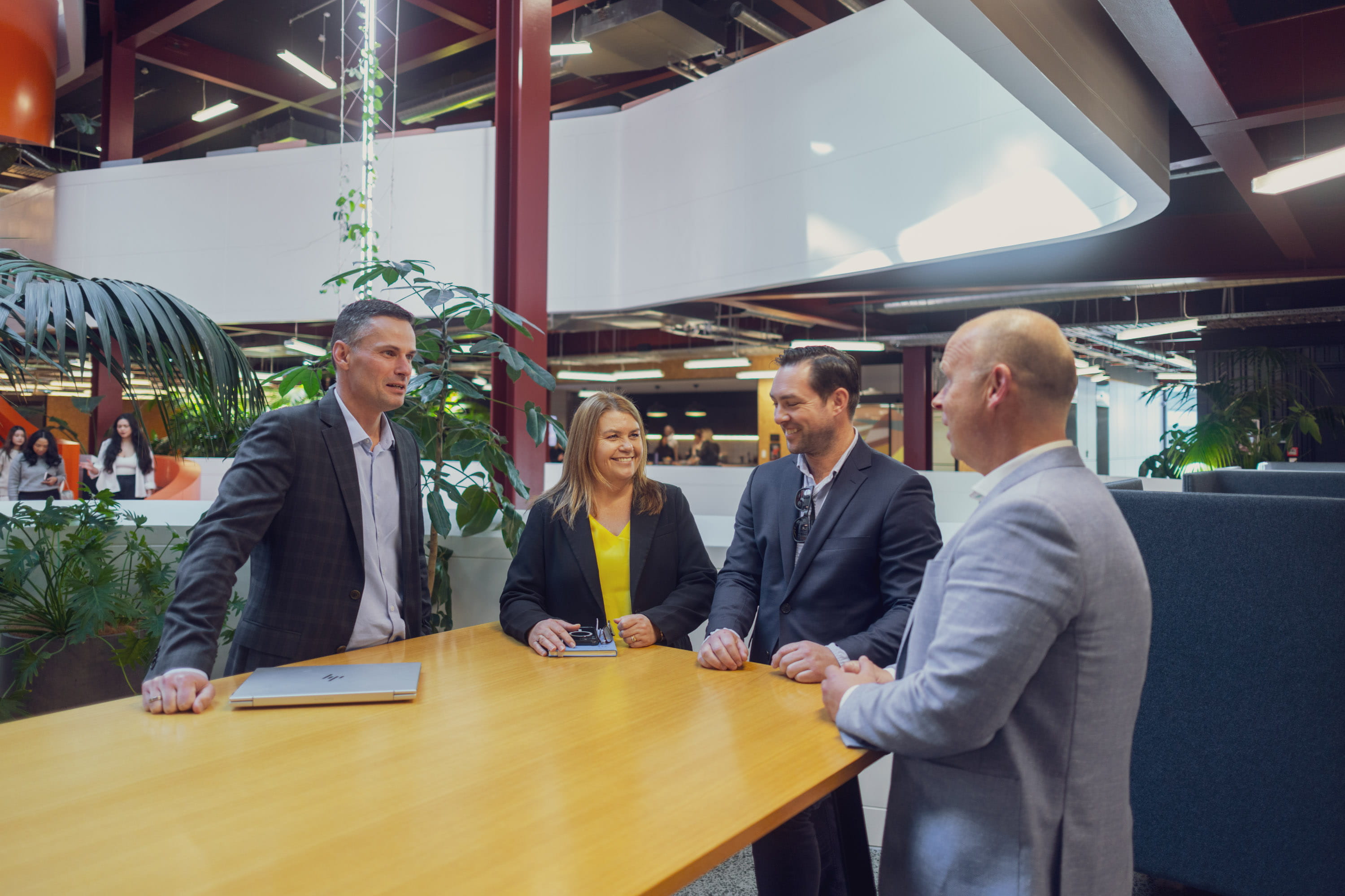 Four of Become Wealth's financial advisers, standing at a table, laughing, discussing a career break one of them is about to take