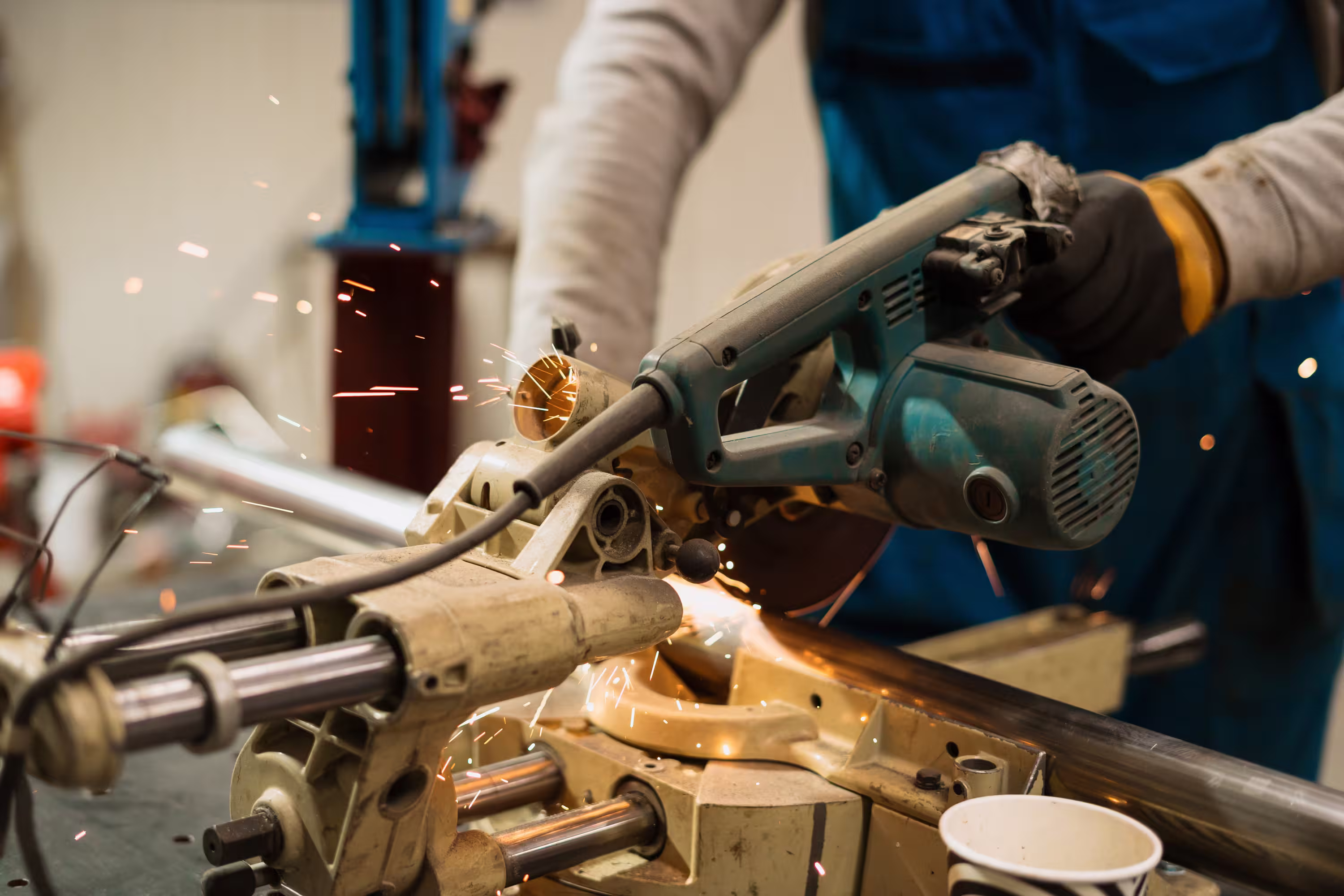 Worker using a power saw to cut metal pipe with sparks flying in a workshop.