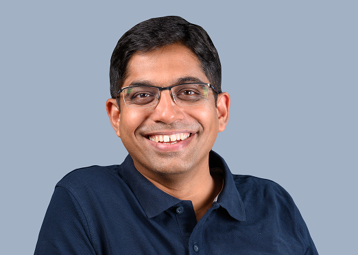 Smiling man wearing glasses and a navy blue Mocha polo shirt against a plain background.