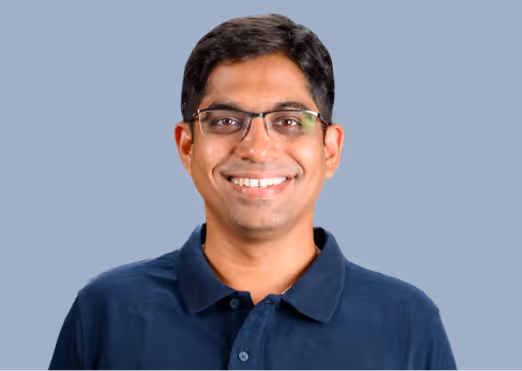 Smiling man wearing glasses and a navy blue polo shirt against a light gray background.