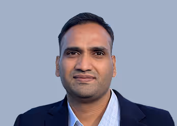 Portrait of a man wearing a dark blazer and light blue shirt against a plain blue background.