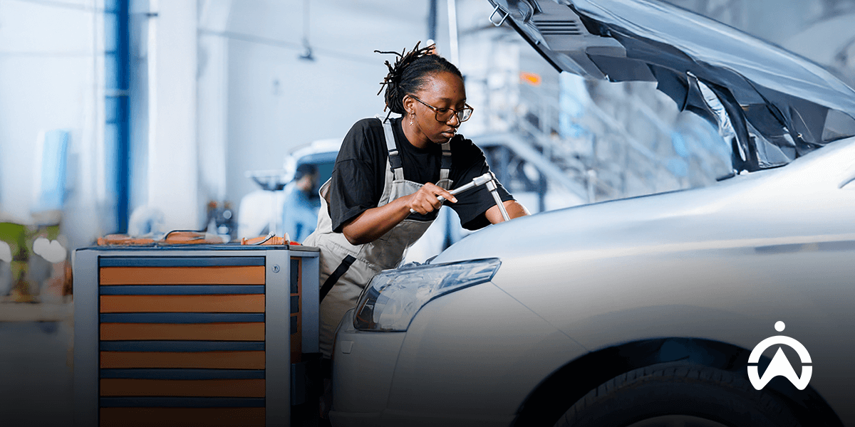 Mechanic with dreadlocks working on a car engine near a tool chest.