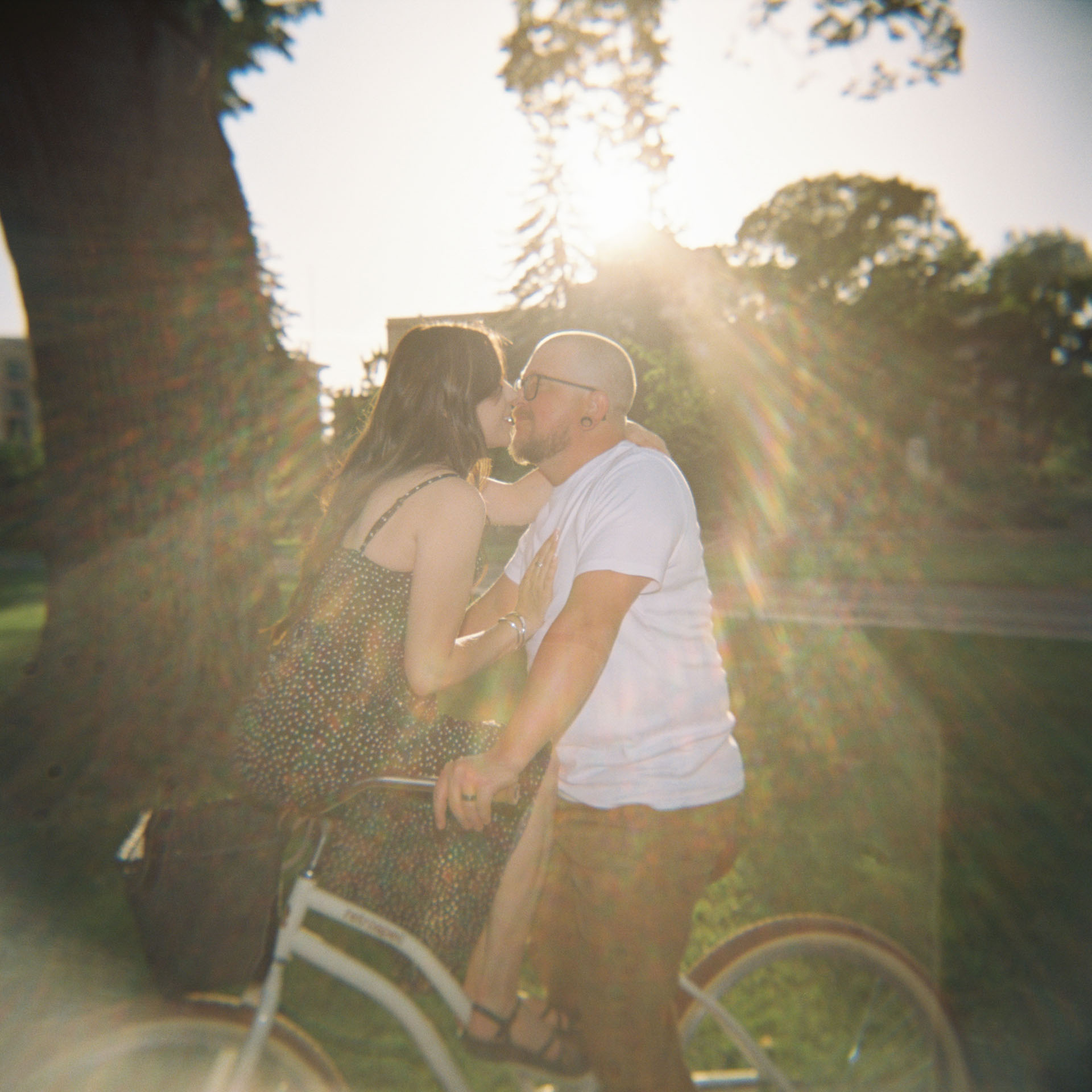 couple kissing while sitting on bike with sun flare