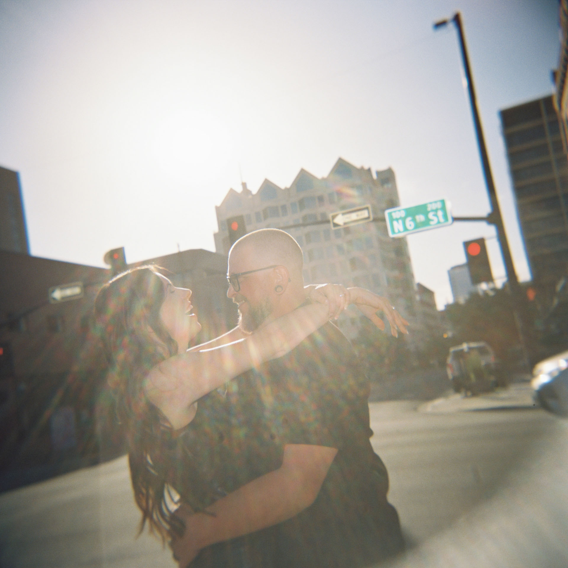 couple laughing along city street with sun flare