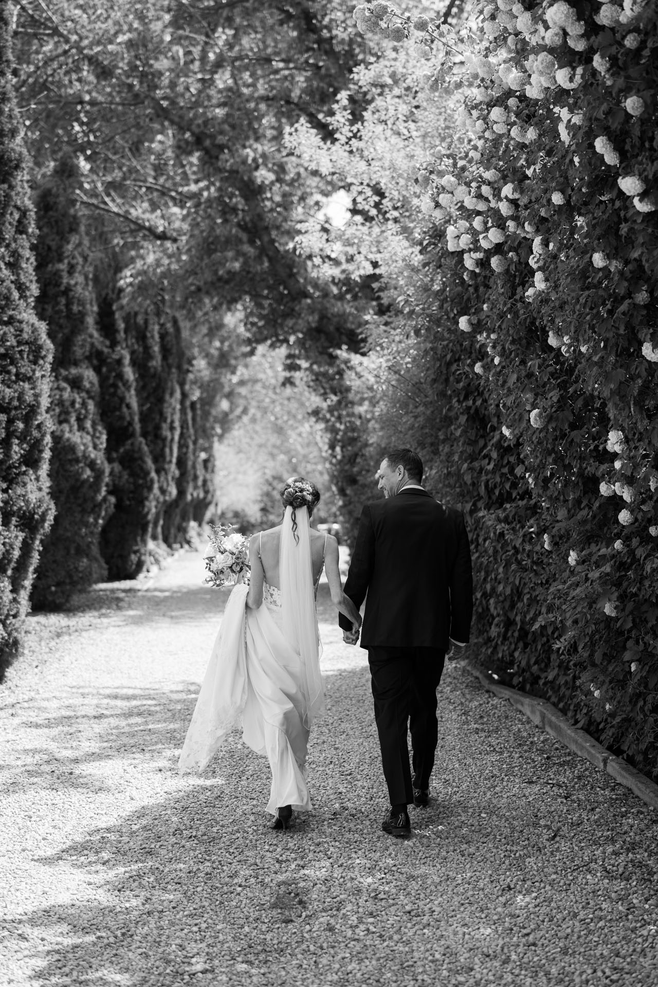 bride and groom walking down a flower lined driveway