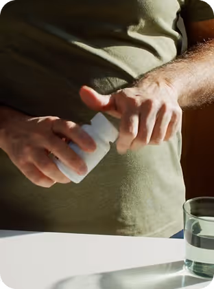 Person opening a white pill bottle near a glass of water