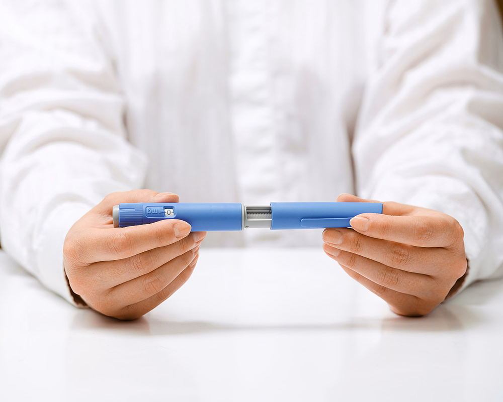 Person holding a disassembled blue insulin pen device with both hands on a white surface.
