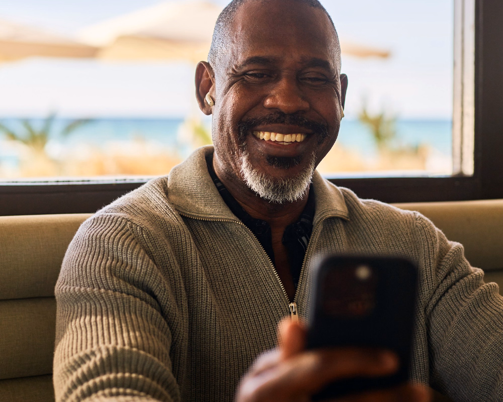 Adult man smiling while using his phone at home, representing convenient online testosterone care through Phoenix Health in Canada.