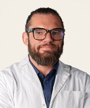 Portrait of Dr. Mark Broussenko, a man with dark hair pulled back, a full beard, and glasses, wearing a white lab coat over a blue shirt.