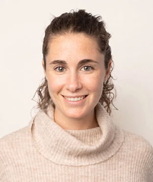 Portrait of Dr. Melissa Goldberg, a smiling woman with curly brown hair pulled back, wearing a beige turtleneck sweater, facing forward.