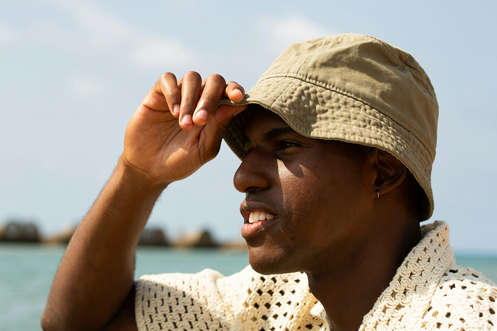 Smiling man in a bucket hat and knit shirt adjusting his brim by the water