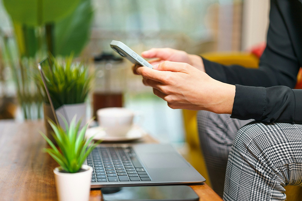 Person using a smartphone at a table beside a laptop and coffee cup, completing an online health assessment