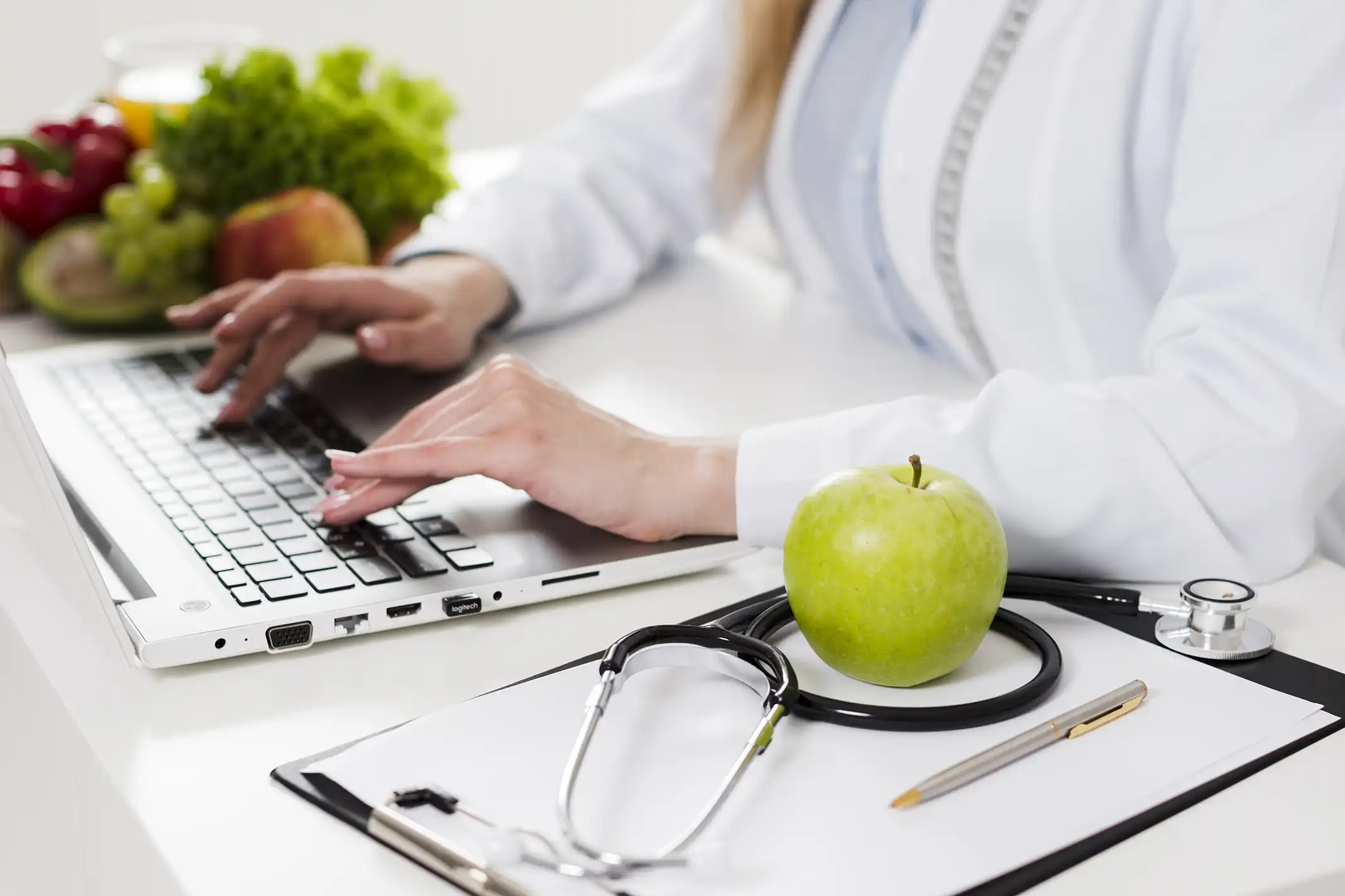 a doctor using laptop, on the table besider her, there are some fruits