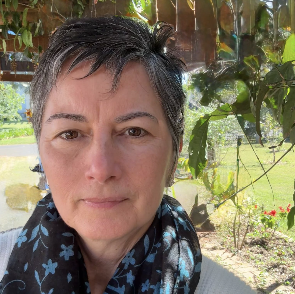 Close-up of a woman with short salt-and-pepper hair wearing a black and blue floral scarf outdoors.