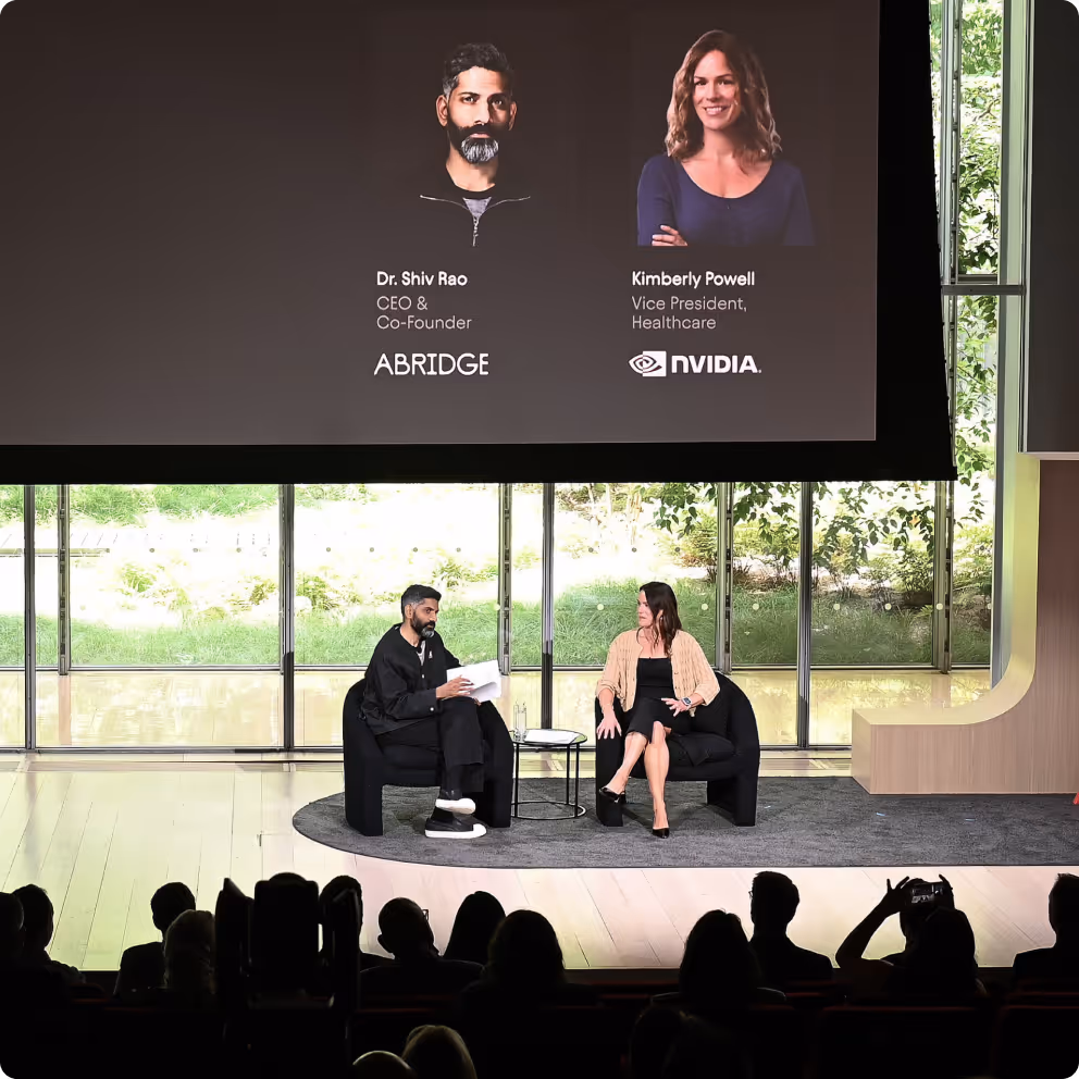 Two people seated on stage engaging in conversation during a keynote presentation with audience silhouettes visible.