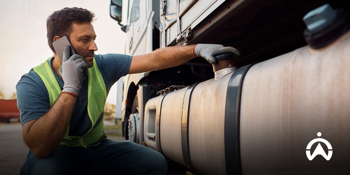 A worker in a green safety vest inspects a fuel tank on a truck, focused on maintenance tasks in a transport yard.