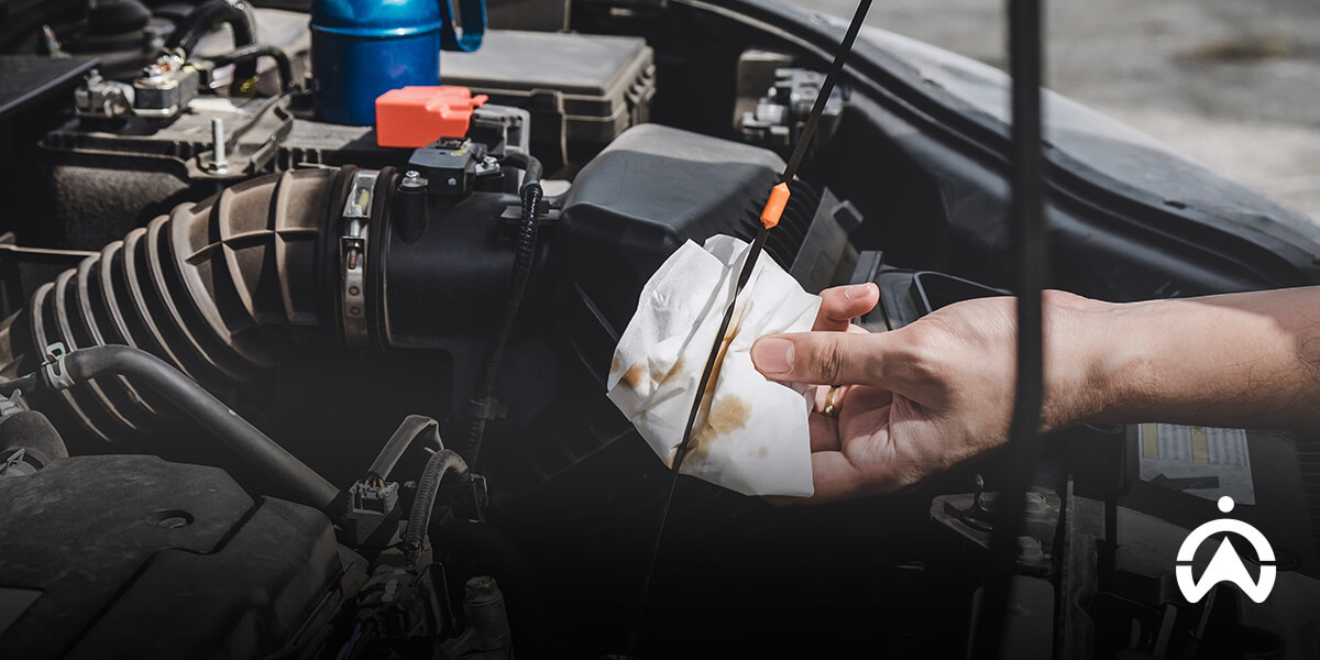 A person checking oil dipstick in a car engine as part of car checks you should never skip before a long road trip.