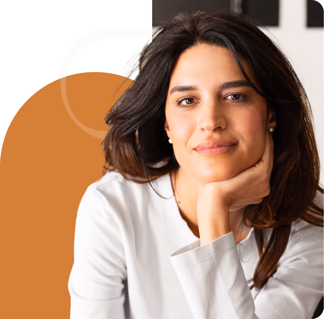 Confident woman with long dark hair resting her chin on her hand, wearing a white blouse, looking directly at the camera with a gentle smile.