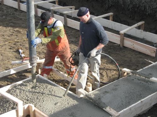 Two people pouring cement into foundation forms.