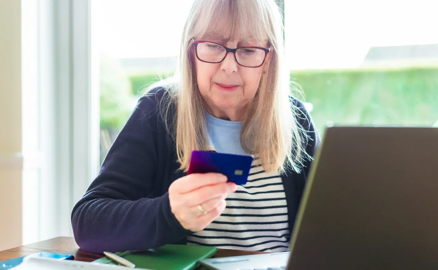 An older woman holding her credit card while staring at a laptop screen