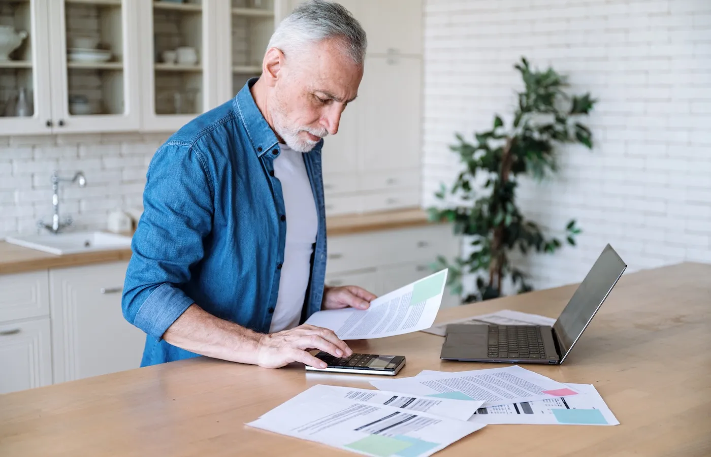 An older man standing over his laptop with bills on the table