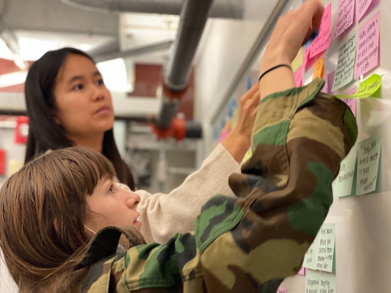 A picture of my teammate Vy and I adding sticky notes to a white board as we affinity map.