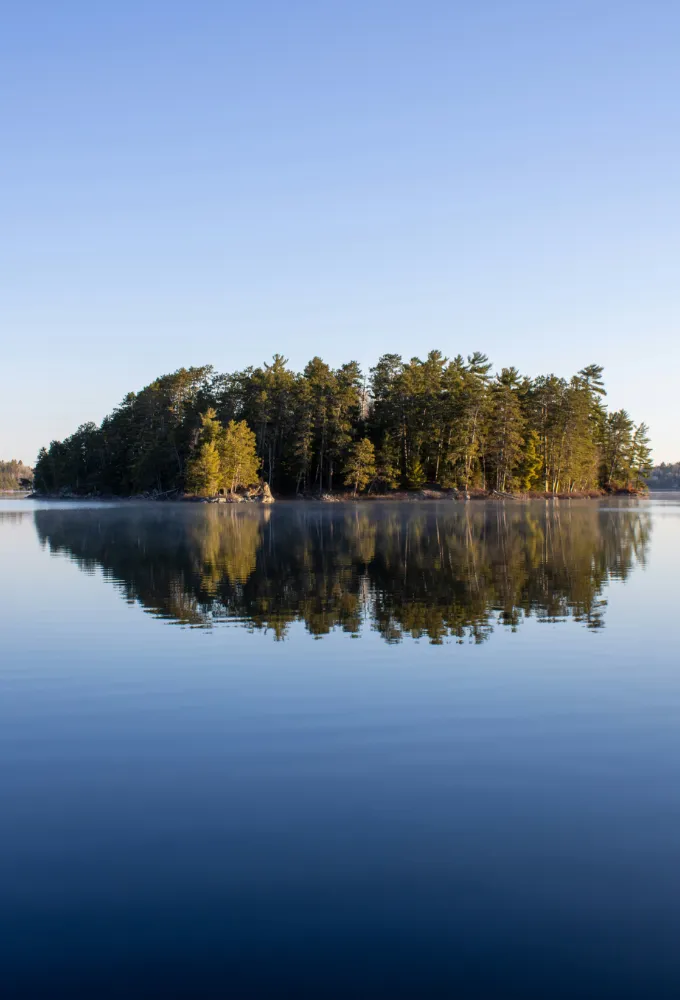 Small island with pine trees reflected in a calm blue lake.