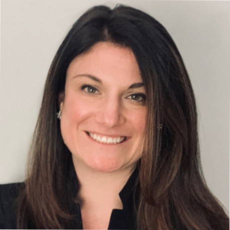 Smiling woman with long brown hair wearing a sleeveless black wrap dress against a black background.