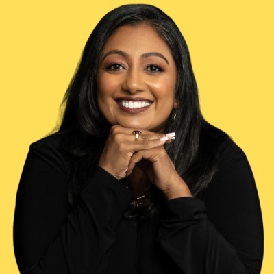Smiling woman with long brown hair wearing a sleeveless black wrap dress against a black background.