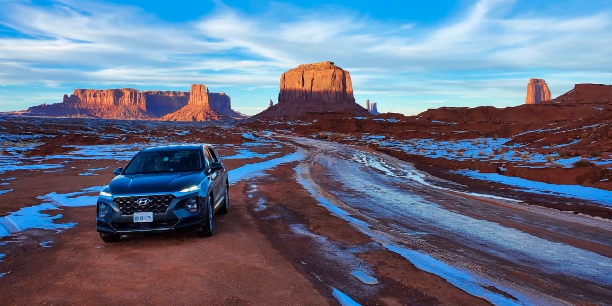 SUV driving a desert road past red rock buttes in Arizona's high desert
