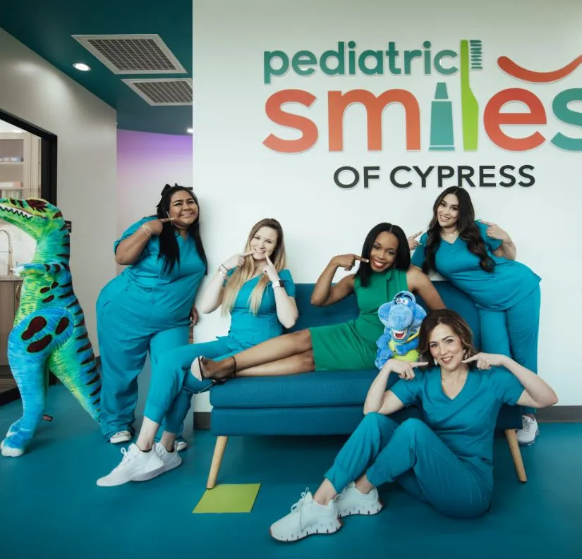Photo of the Pediatric Smiles team sitting on a couch pointing to their smiles