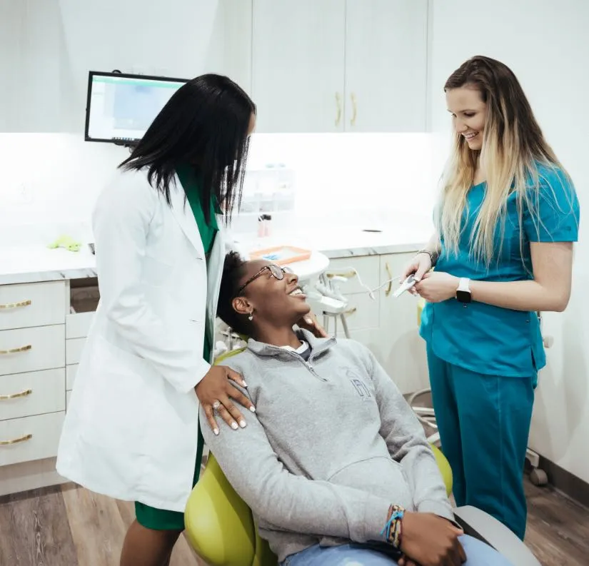 Photo of a patient sitting in an exam chair talking with Dr. Marshall and another dental team member