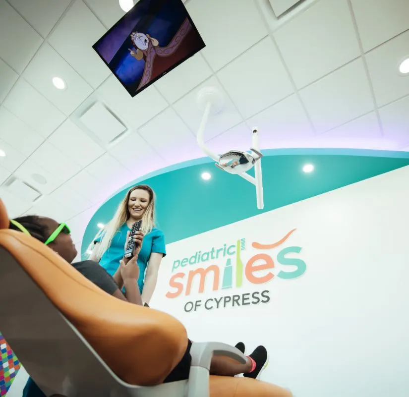 Photo of a relaxed kid wearing sunglasses reclining in a dental chair while watching a movie